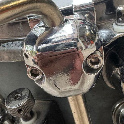 A chrome clamp with two hex bolts gripping the snare hoop, with a knurled rod running down from it.