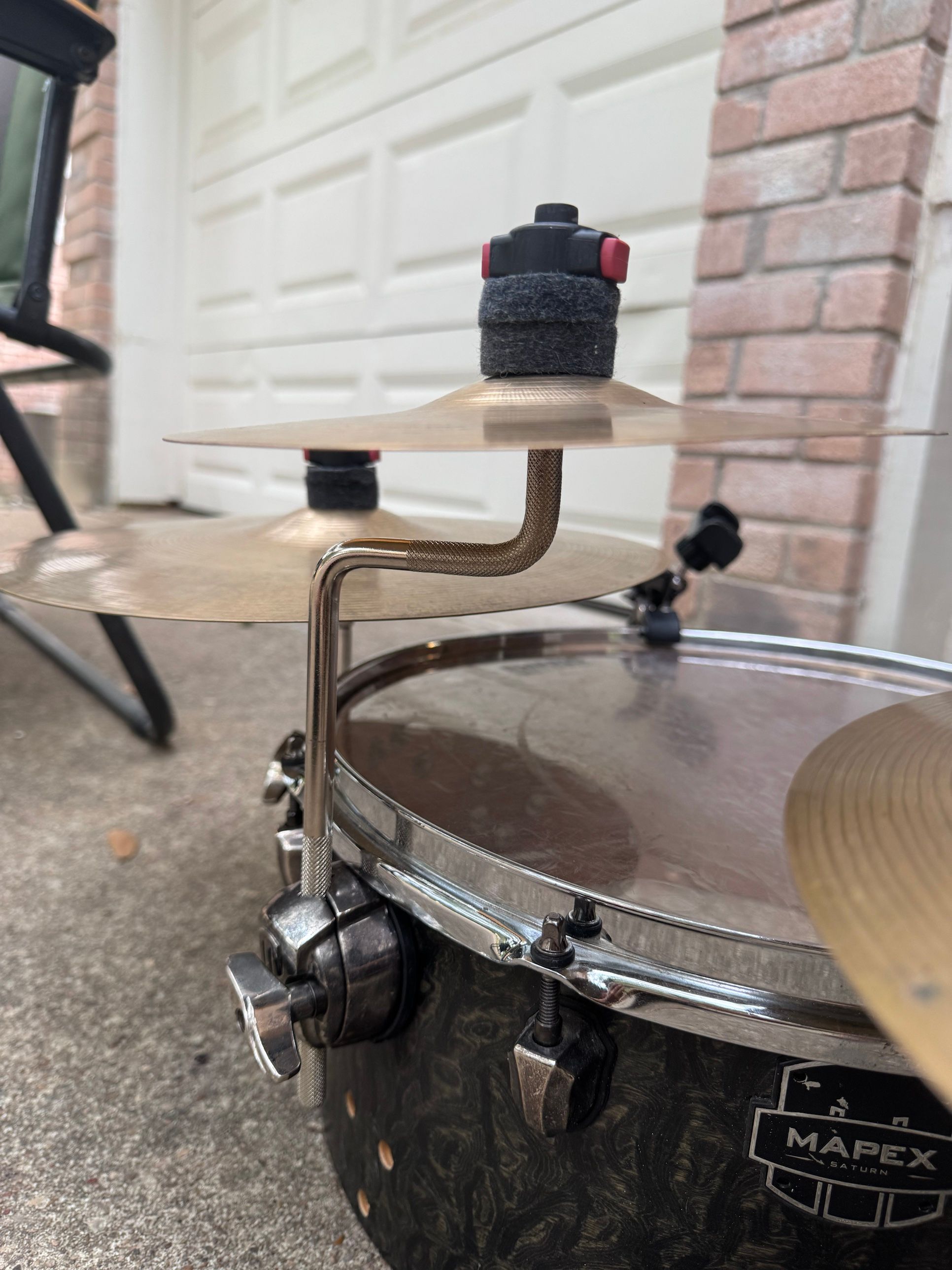 A knurled Z-shaped arm rising from the floor tom’s leg mount and holding a small cymbal.