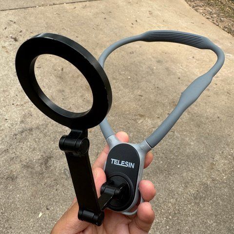 A grey TELESIN neck mount with a black magnetic phone ring, held in a hand.