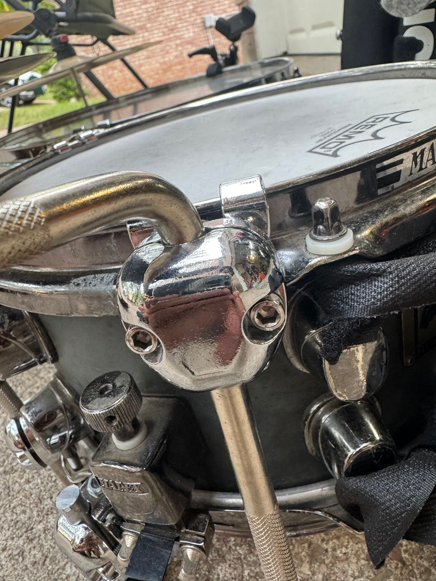 A chrome clamp with two hex bolts gripping the snare hoop, with a knurled rod running down from it.