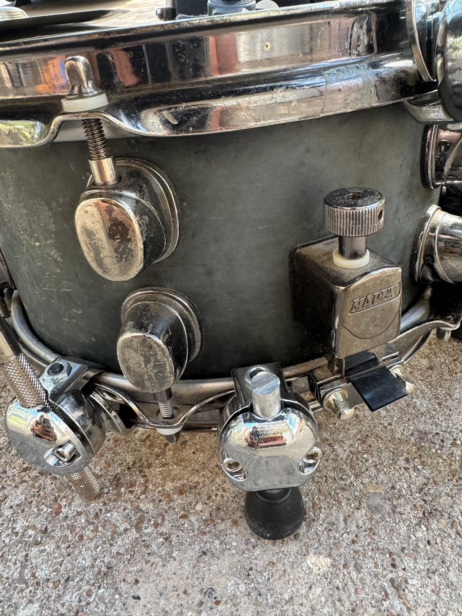 Close-up of the lower snare shell, with chrome hoop clamps on the bottom hoop holding short legs with rubber feet.