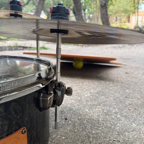 A straight cymbal stacker rod standing in the floor tom’s leg mount, holding a cymbal above the drum.