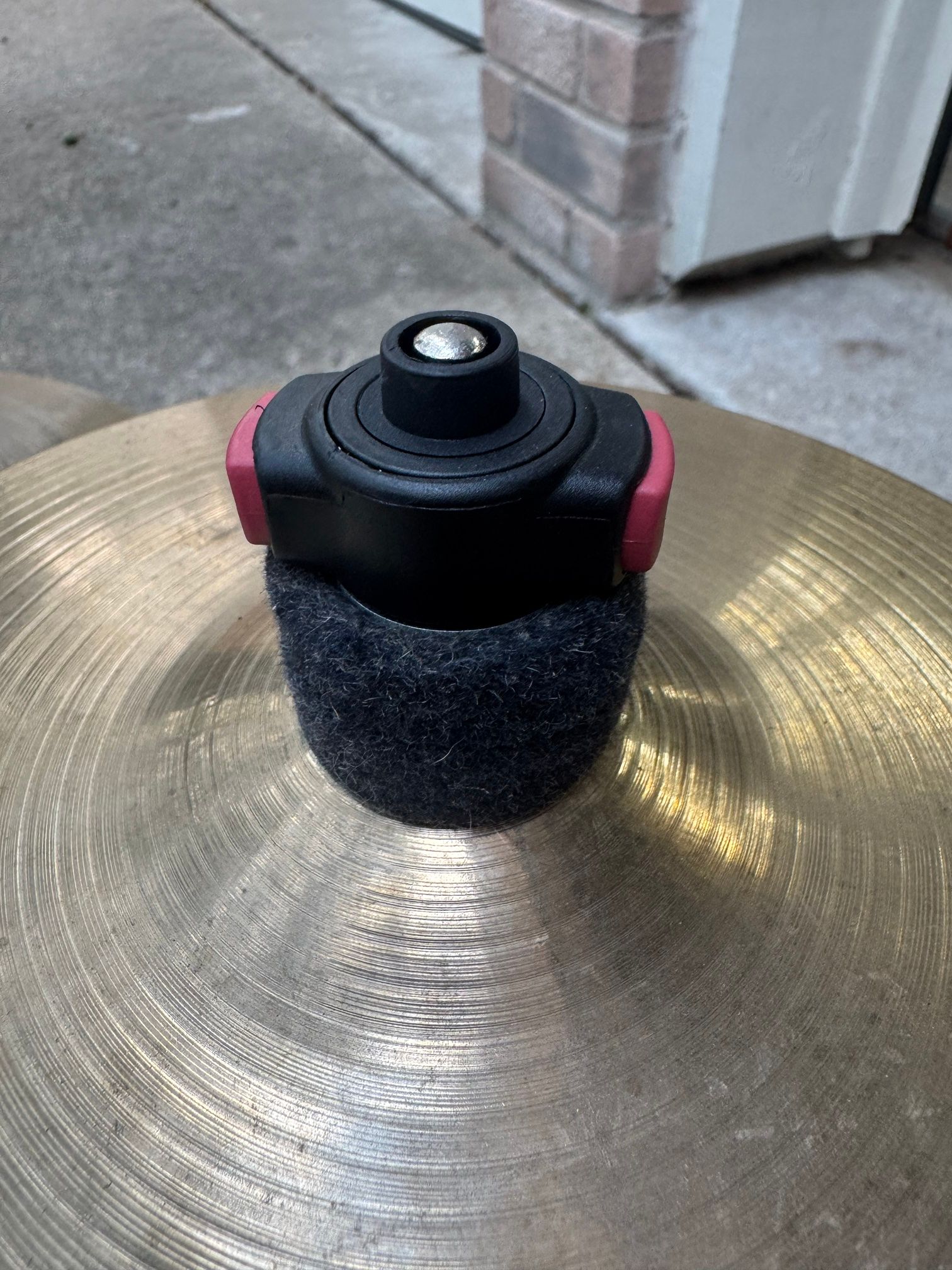 A black quick-set cymbal nut with red release tabs and a felt sleeve, on a cymbal bell.